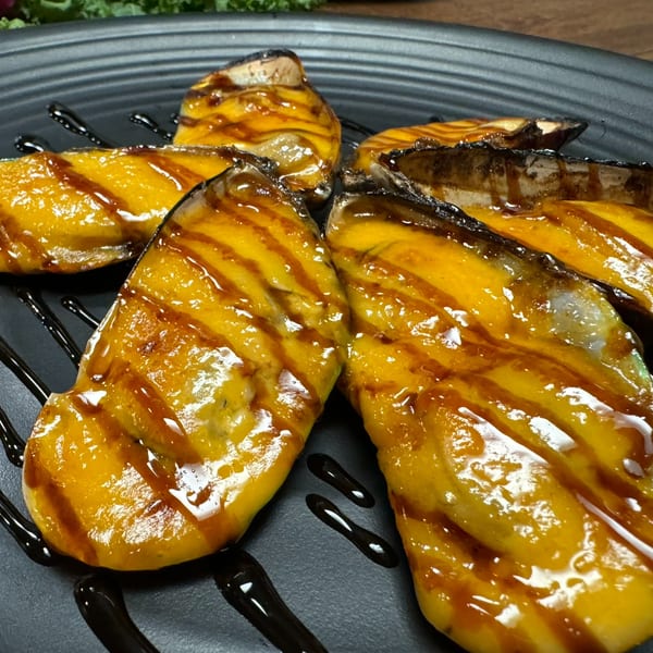 Grilled mussels with a sweet glaze and balsamic drizzle on a black plate at Ninja Sushi & Hibachi.