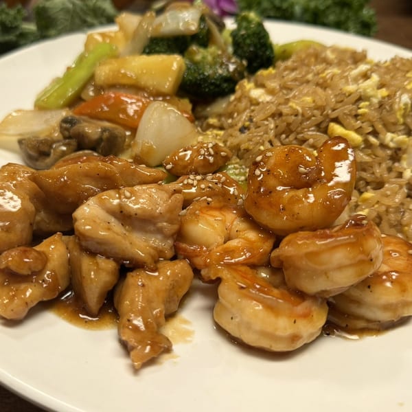 Hibachi chicken and shrimp with fried rice and mixed vegetables on a white plate.