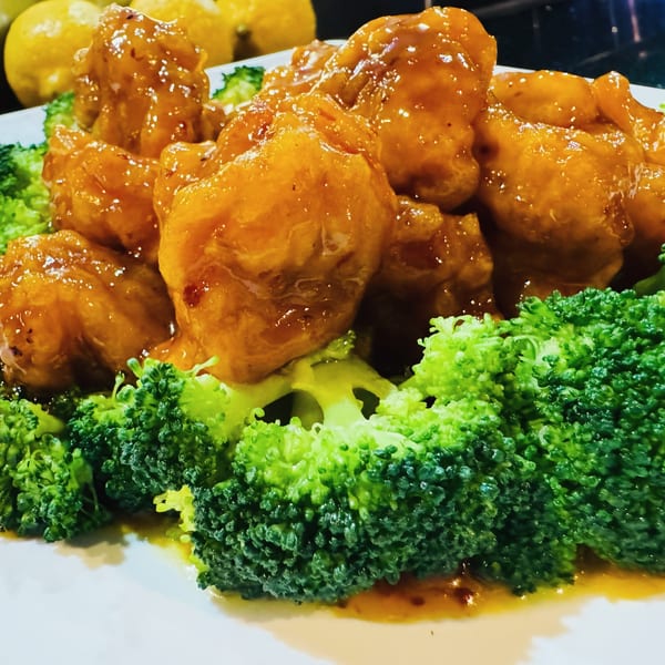 Orange chicken with a glossy sauce and fresh green broccoli florets on a white plate.